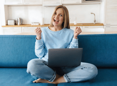 A woman sitting on a couch, working on her laptop, with a focus on finding legitimate online jobs that pay daily.