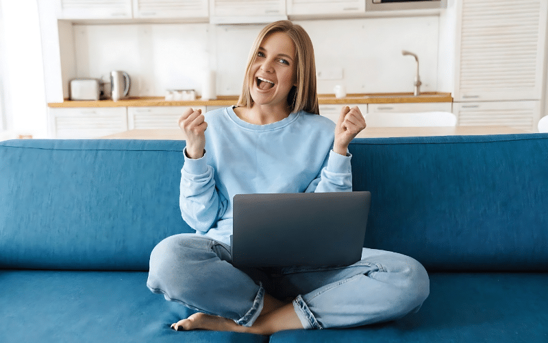 A woman sitting on a couch, working on her laptop, with a focus on finding legitimate online jobs that pay daily.