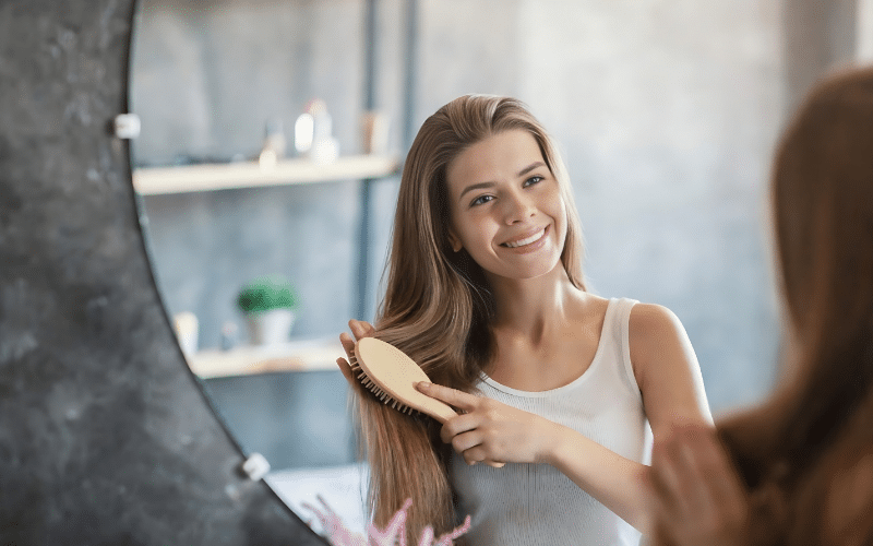 A woman brushing her hair in front of a mirror, promoting solutions to stop hair fall and encourage hair regrowth.