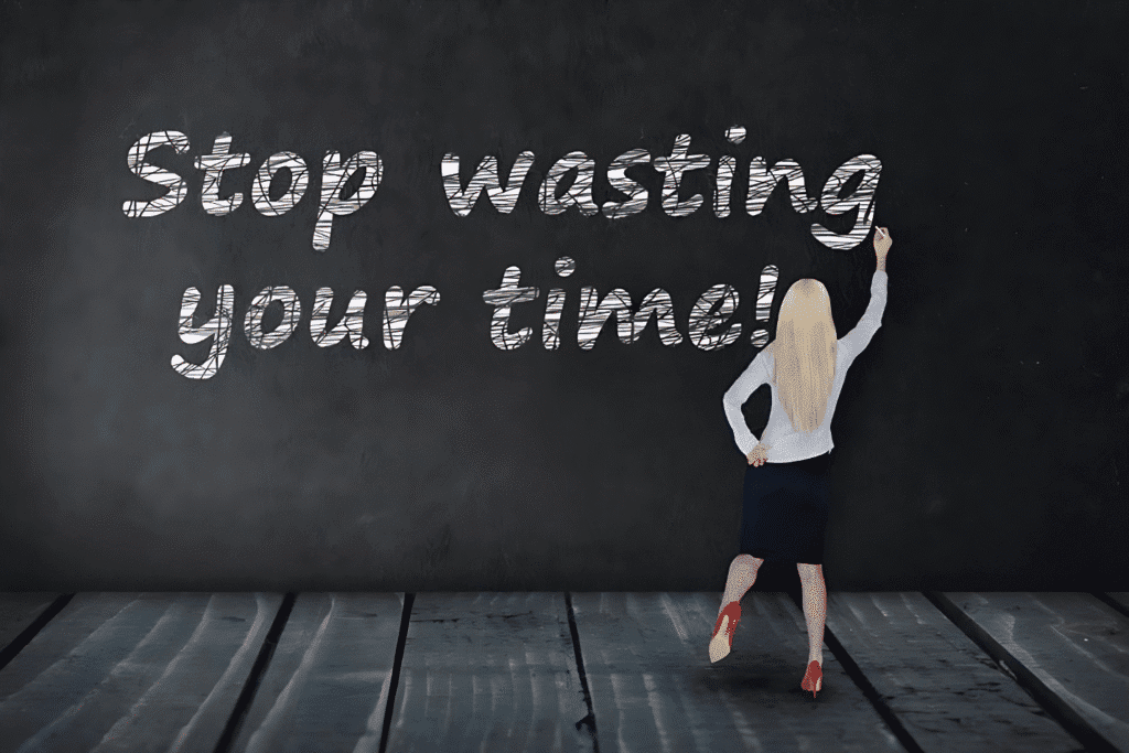 A woman writes "Stop wasting your time" on a blackboard, emphasizing the message to use time wisely.