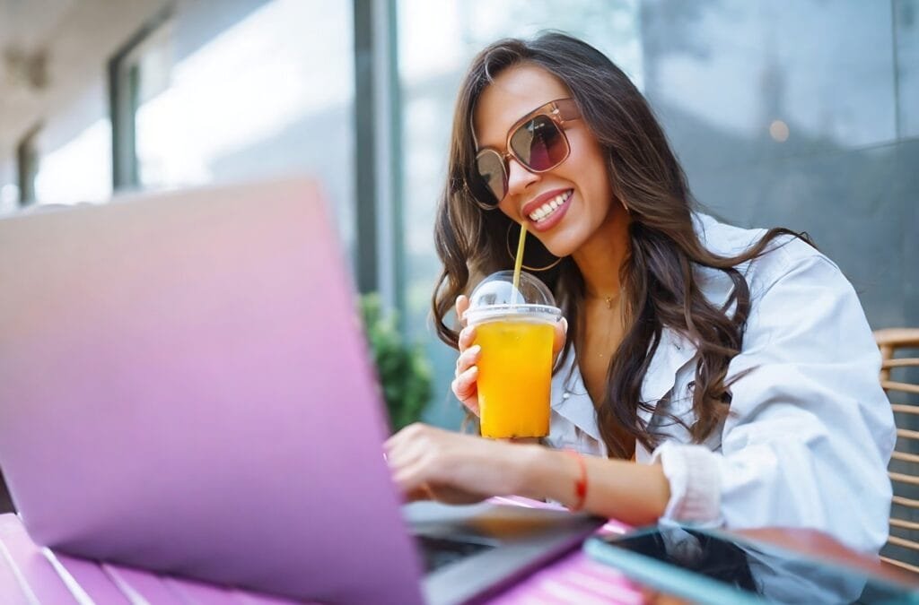 A woman wearing sunglasses sits at a table, working on a laptop, focused on creating successful pins.