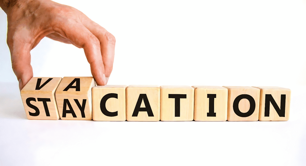 A hand grips a block reading "vacation," representing creative staycation concepts and leisure time.