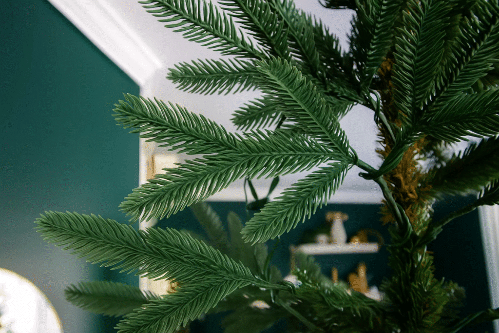 An artificial green Christmas tree with lush leaves stands beside a decorative mirror.