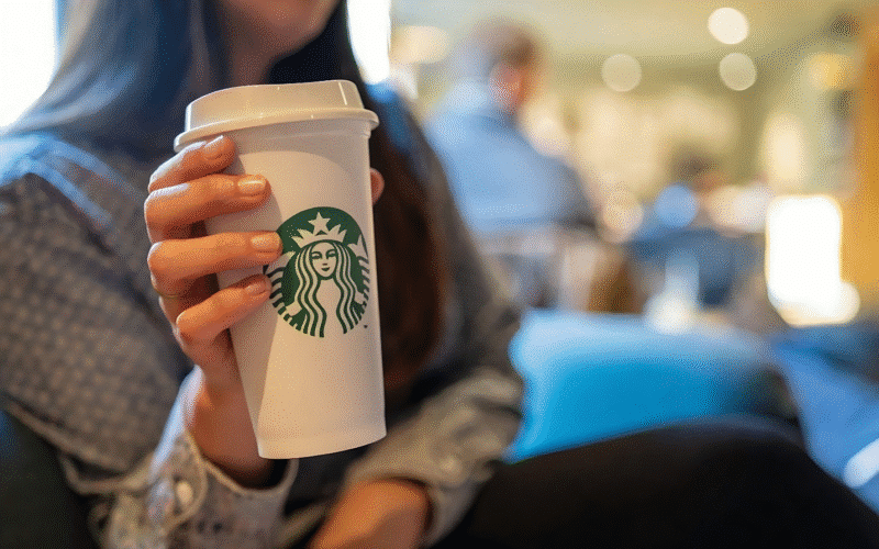 A woman holding a Starbucks cup, showcasing the cheapest drink option available at the coffee shop.