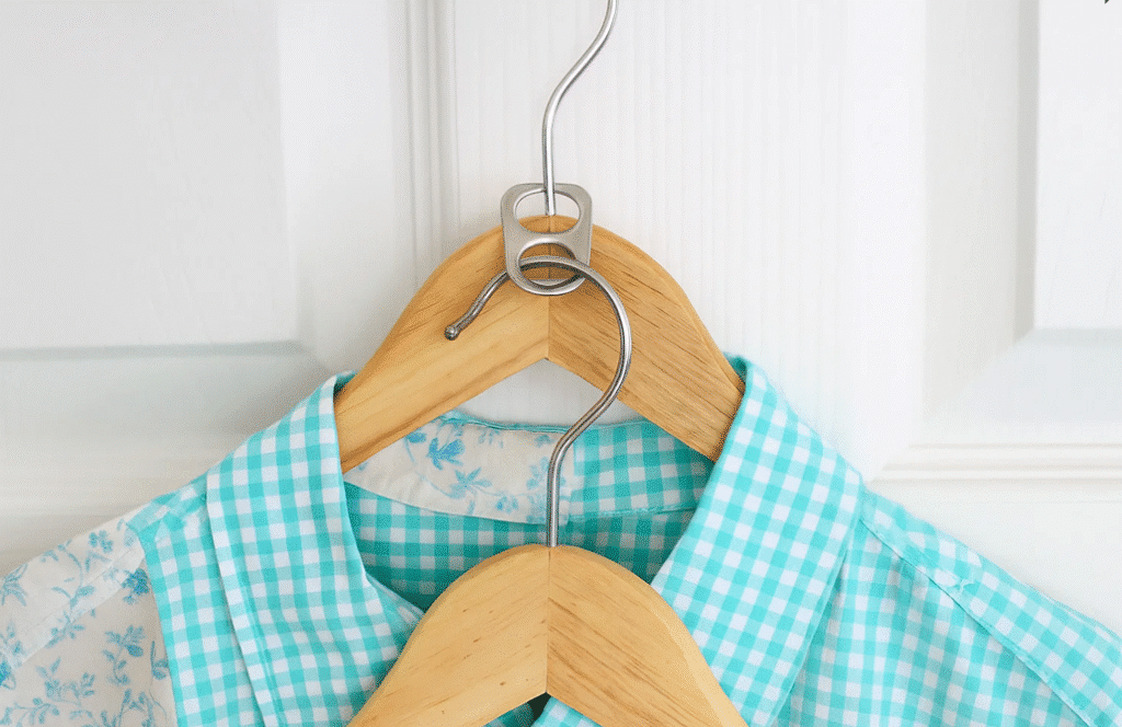 A shirt is hanging on a wooden hanger attached to a door, with soda can tabs used to hook the hangers together.