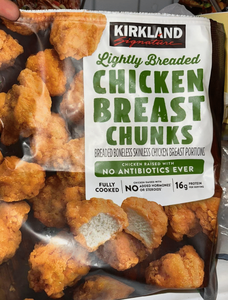 A bag of Kirkland Lightly Breaded Chicken Breast Chunks, featuring text that highlights the product's attributes such as "breaded boneless skinless chicken breast portions," "raised with no antibiotics ever," and "fully cooked with no added hormones or steroids." The bag is presented in a snack food context.