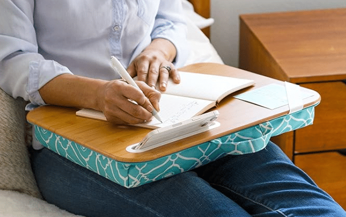 A woman on a bed, focused on writing in a notebook with a lap desk, creating a cozy and productive workspace.