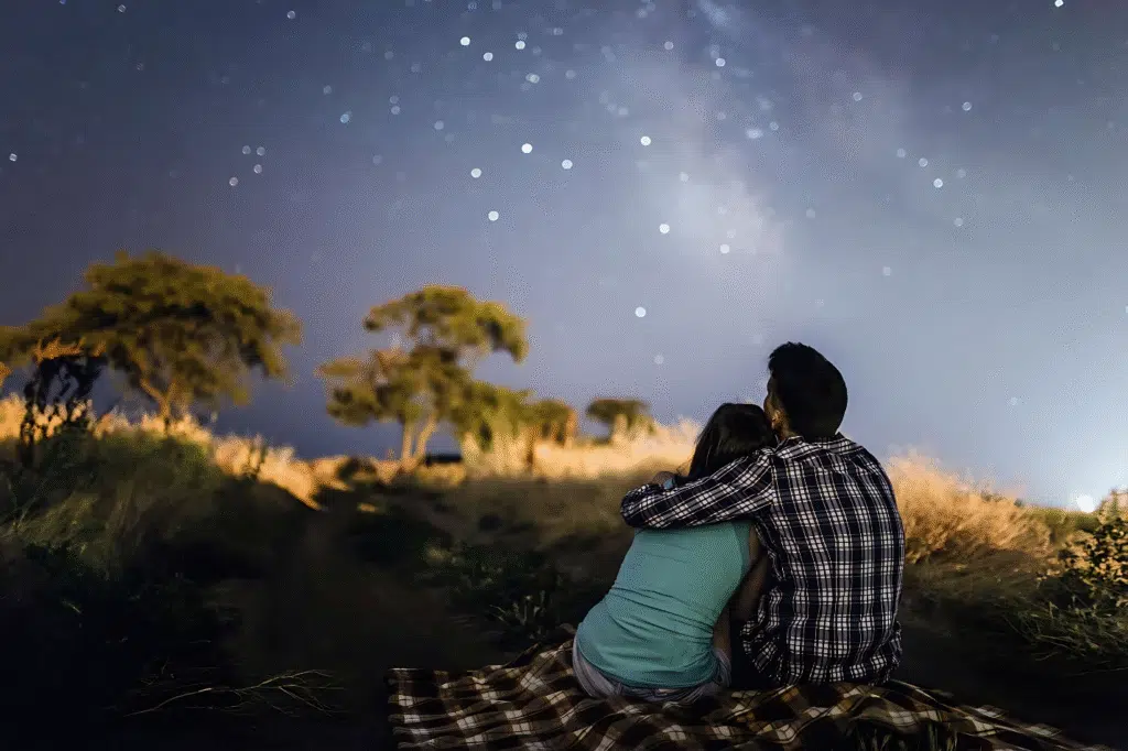 Couple sitting on a blanket, gazing at a starry sky during a romantic stargazing date.