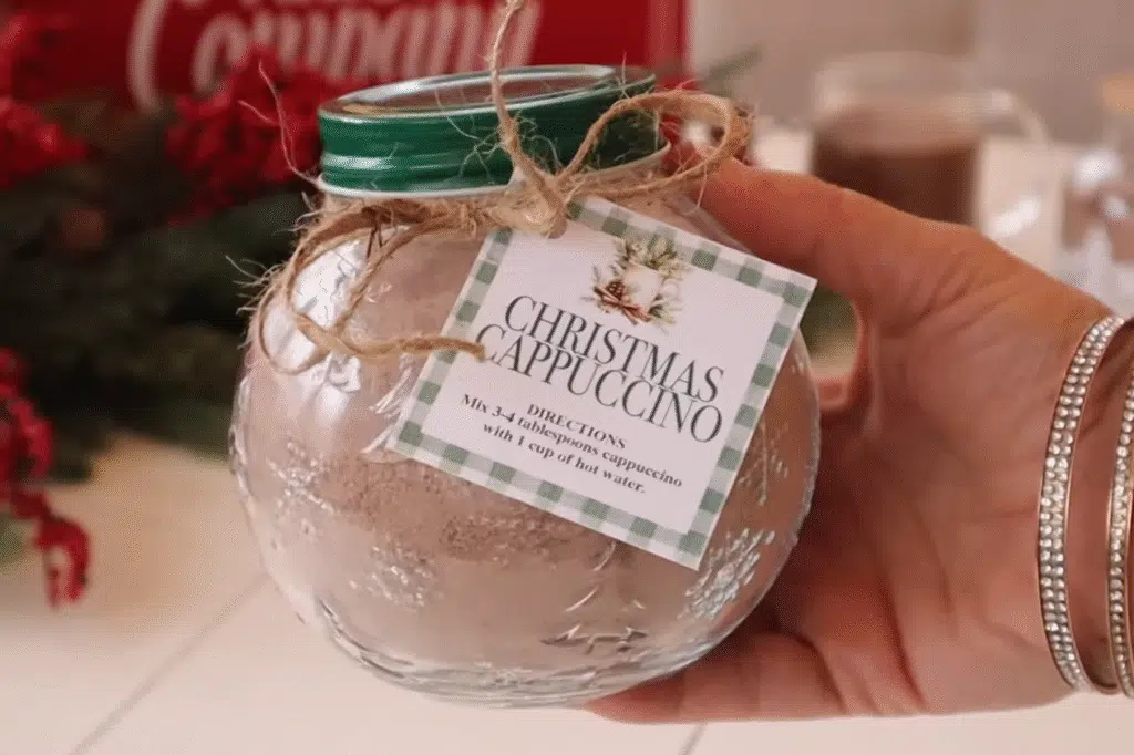 A hand presents a jar of Christmas Cappuccino Mix against a backdrop of a beautifully adorned Christmas tree.