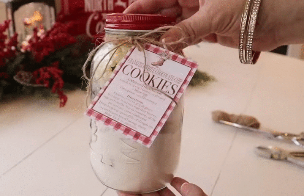 A person holds a jar of Cranberry White Chocolate Cookies in front of a decorated Christmas tree.