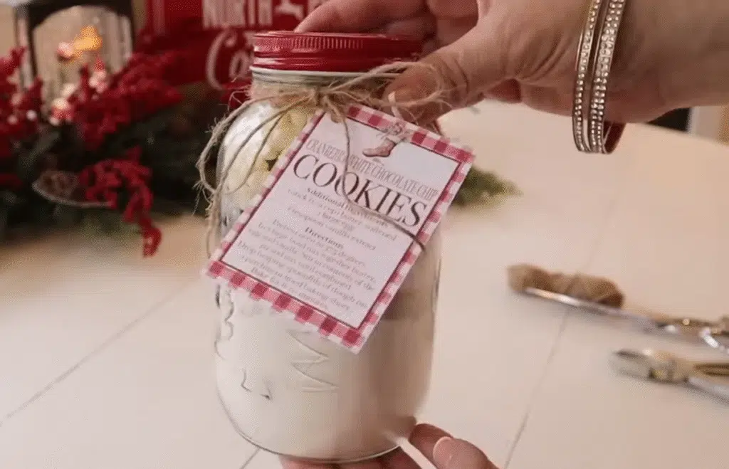 A person holds a jar of Cranberry White Chocolate Cookies in front of a decorated Christmas tree.