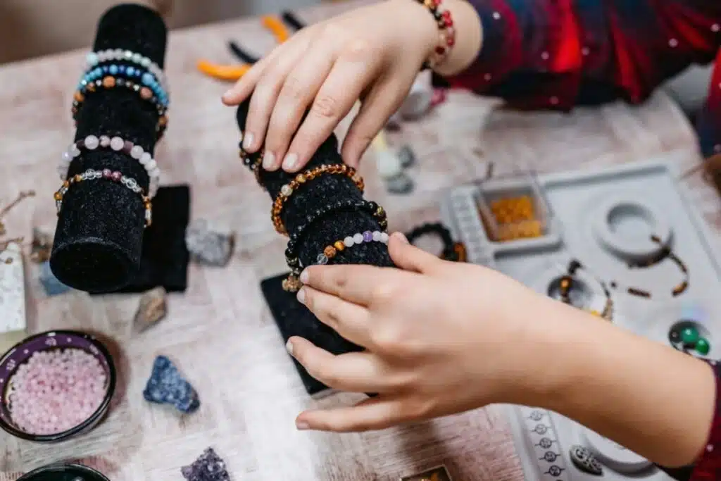 A person's hands with neatly manicured nails holding multiple bracelets and a watch, showcasing fashion accessories indoors.