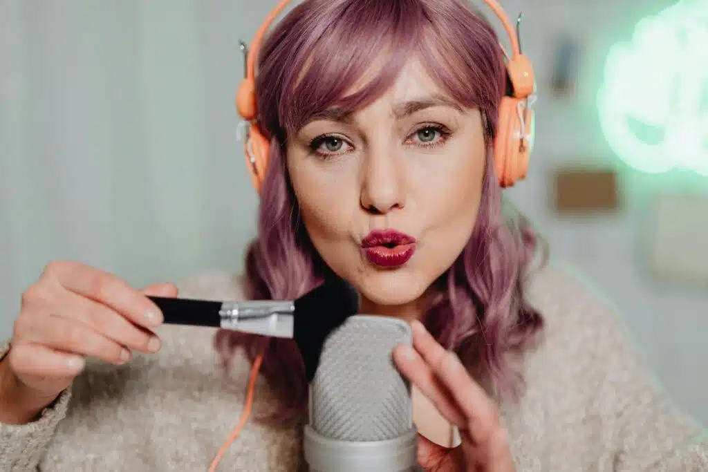 ASMR YouTube creator wearing headphones whispering into a microphone and brushing it, recording relaxing niche content.