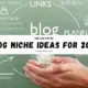 Hands holding a glowing light bulb with brainstorming words like links, ideas, and creativity in background suggesting blog niche ideas for 2026.
