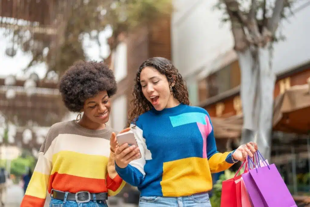 Two young women shopping together, focused on their cell phone, possibly discussing items from a Buy Nothing Group.