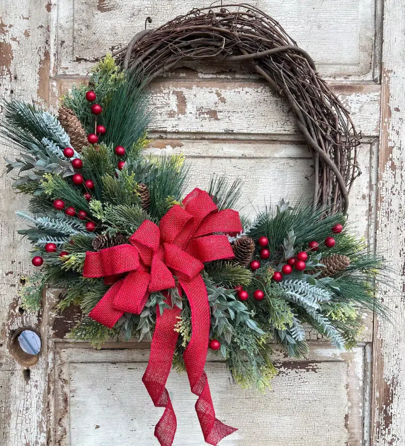 A Christmas wreath featuring vibrant red berries and pine cones, elegantly displayed on a front door.