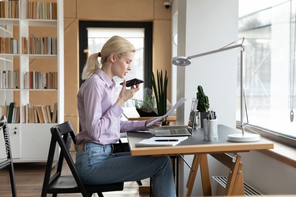 A woman at her desk using a laptop and cell phone, engaged in a skill assessment activity.