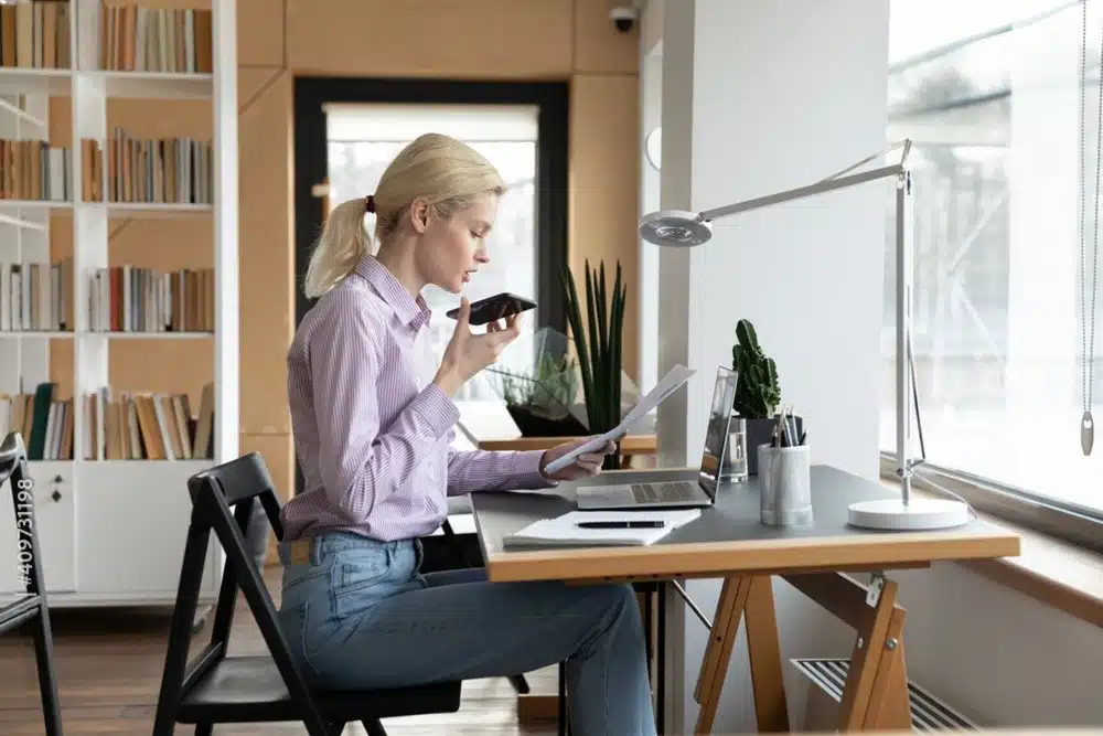A woman at her desk using a laptop and cell phone, engaged in a skill assessment activity.