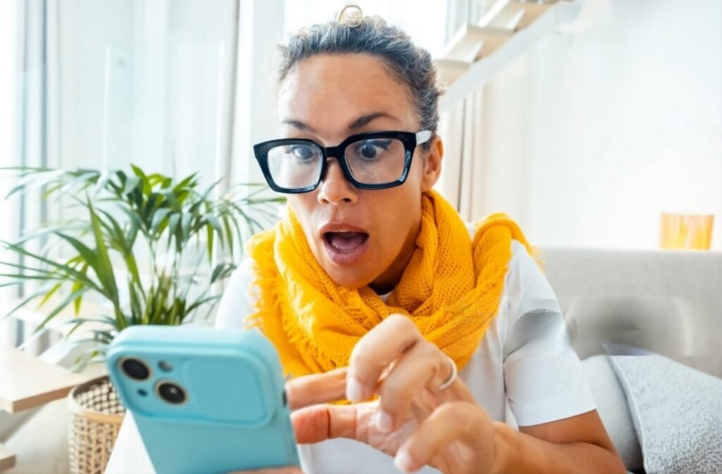 Shocked woman with big glasses and yellow scarf looking at her smartphone, reacting to surprising YouTube video titles.