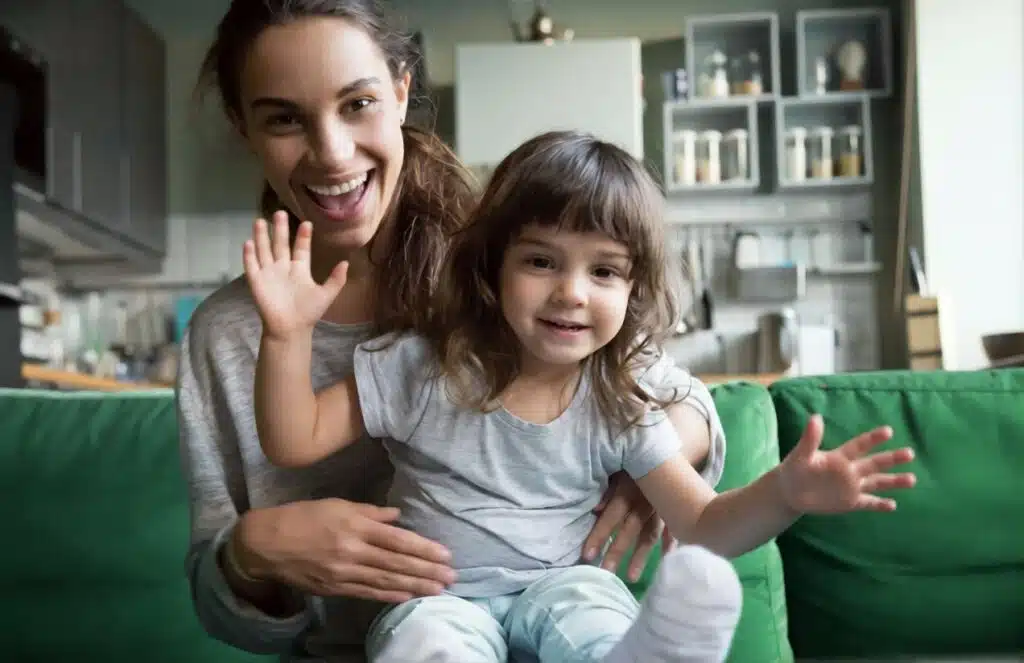 Smiling mom and toddler waving on a green couch, lifestyle photo for choosing a mom blog name