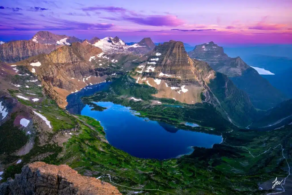 The sun sets over the mountains and lake in Glacier National Park, casting warm hues across the serene landscape.