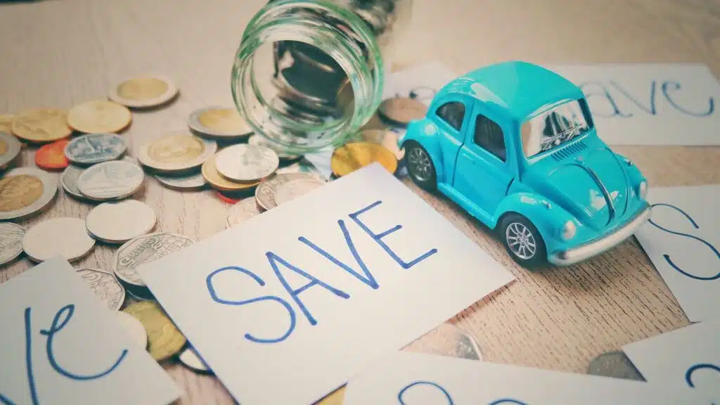 Coins spilling from a savings jar, a toy car, and a note reading “SAVE,” symbolizing transportation and expense awareness in How to Budget and Save Money effectively.