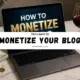 laptop on desk showing how to monetize a blog with money, showcasing behind wine glass, and workspace setup.