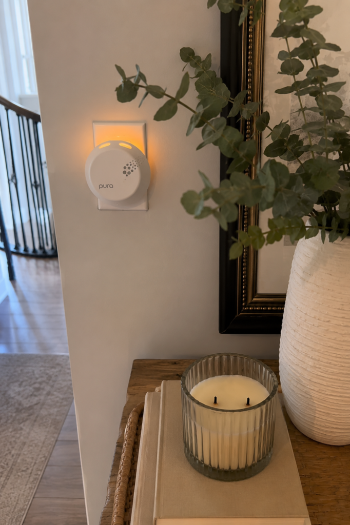 Pura smart diffuser plugged into a wall beside home décor